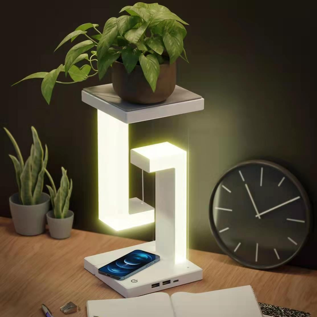 Modern desk lamp with phone charging station on a wooden surface with plants and a clock.
