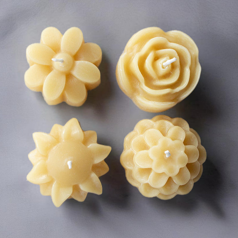 Four floral-shaped candles on a gray background